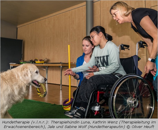 Mädchen im Rollstuhl mit Therapiehund und Therapeuten