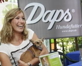 Christine Theiss mit kleinem Hund vor ein Plakat von Daps